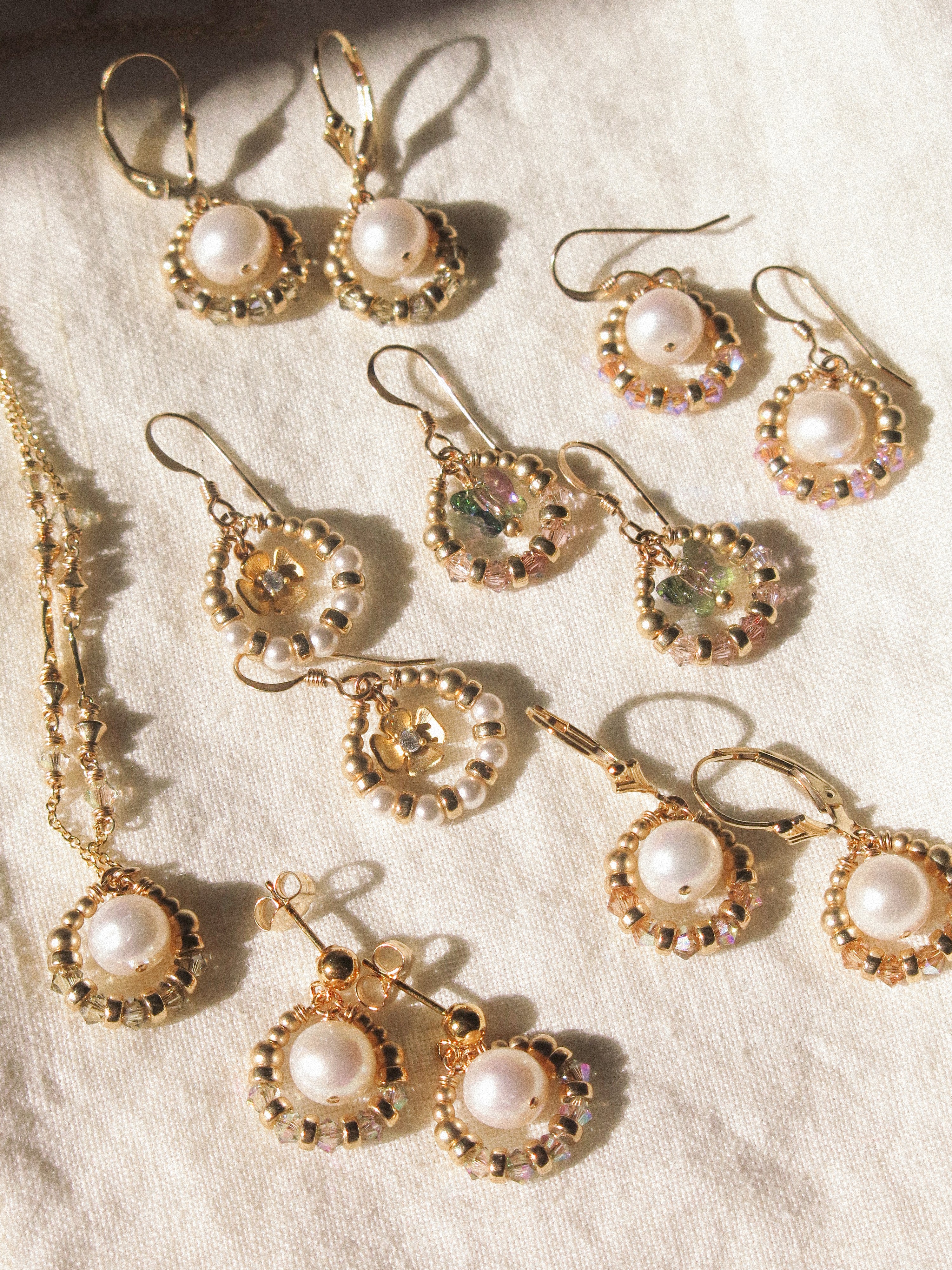 Set of gold earrings with pearls on a textured beige surface
